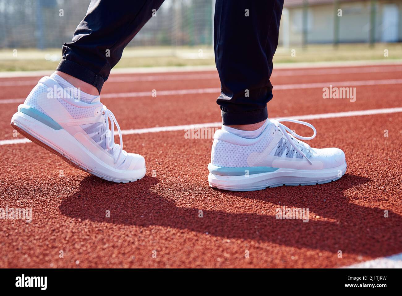 Männliche Läuferfüße mit weißen Sneakers auf der Stadionstrecke, Nahaufnahme. Sport-Sneaker zum Joggen. Fitness und gesundes Lifestyle-Konzept Stockfoto