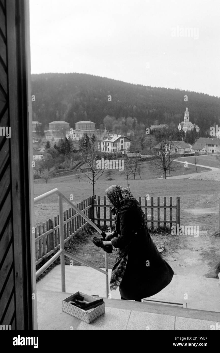 Frau beim Schuhputzen mit Blick auf den Bayerischen Wald im Zwieseler Umland, 1958. Frau, die Schuhe putzt, mit Blick auf den Bayerischen Wald am Stadtrand von Zwiesel, 1958. Stockfoto
