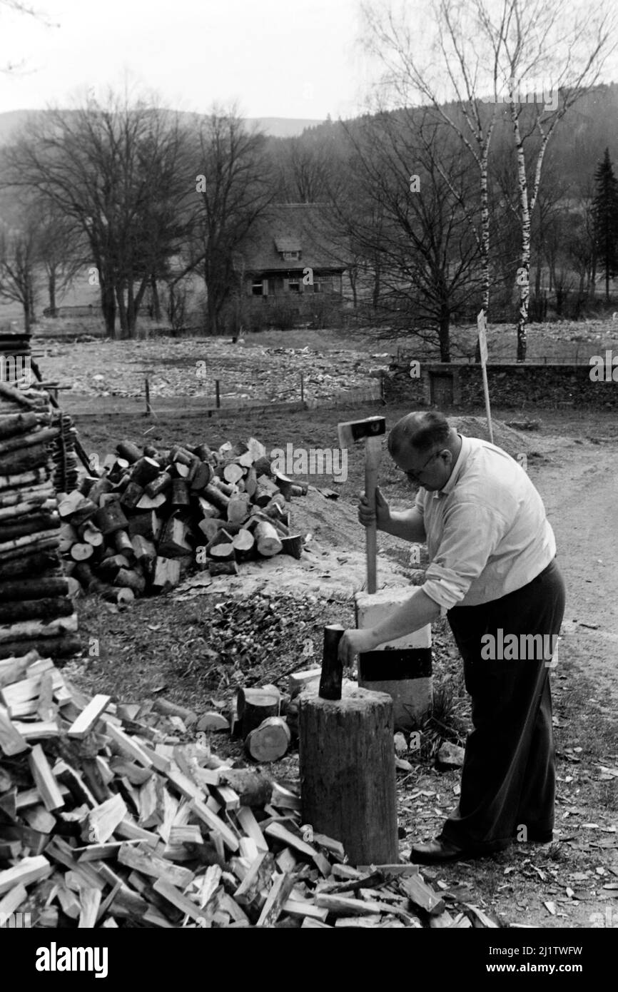 Mann hackt Feuerholz in Bayerisch Eisenstein an der deutsch-tschechischen Grenze, 1958. Man hackt Brennholz in der Stadt Bayerisch Eisenstein nahe der deutsch-tschechischen Grenze, 1958. Stockfoto