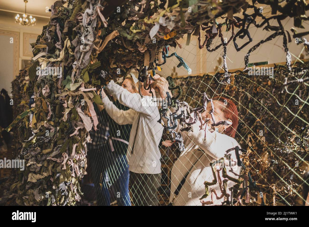 LVIV, UKRAINE - 17. März 2022: Freiwillige weden Tarnnetz für die ukrainischen Streitkräfte. Handgefertigtes Maskennetz aus naturfarbenen Teppichen Stockfoto