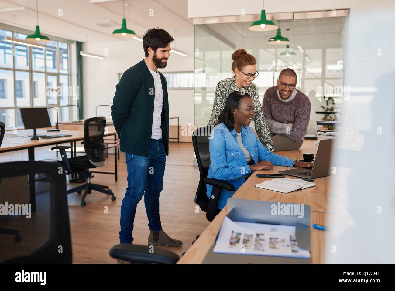 Lächelnde Gruppe verschiedener Geschäftsleute, die um einen Laptop herum zusammenarbeiten Stockfoto