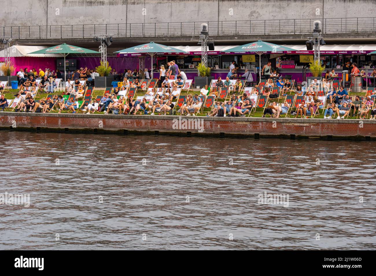 Berlin, Deutschland - 7. August 2021: Die Menschen entspannen sich auf Liegestühlen und Bars am Ufer der Spree im zentralen Bezirk Mitte der Stadt, in der Nähe Stockfoto