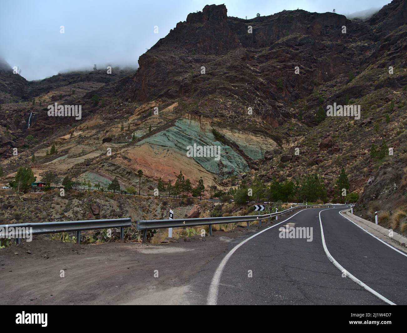 Berg mit bunten vulkanischen Felsen bei Los Azulejos De Veneguera im Westen von Gran Canaria, Kanarische Inseln, Spanien am bewölkten Tag mit Landstraße. Stockfoto