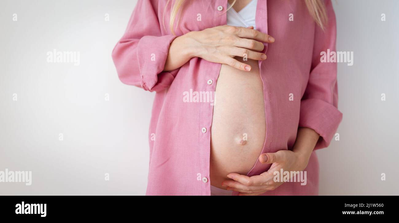 Eine Schwangere in Unterwäsche und einem rosa Hemd steht auf weißem Hintergrund Stockfoto