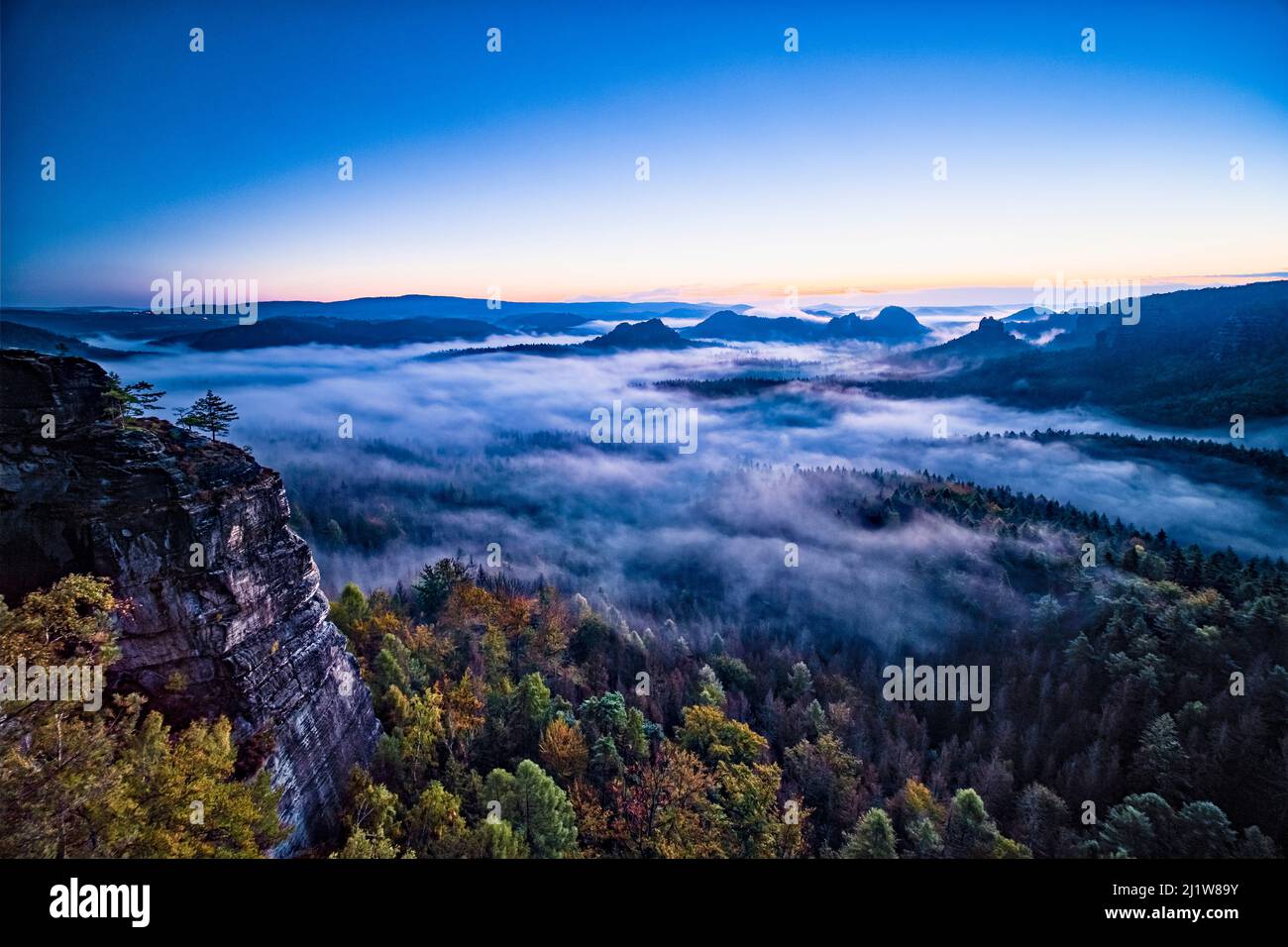 Landschaft mit Felsformationen und dem Gipfel Winterstein im Zschand Gebiet des Nationalparks Sächsische Schweiz bei Sonnenaufgang in Nebel gehüllt. Stockfoto
