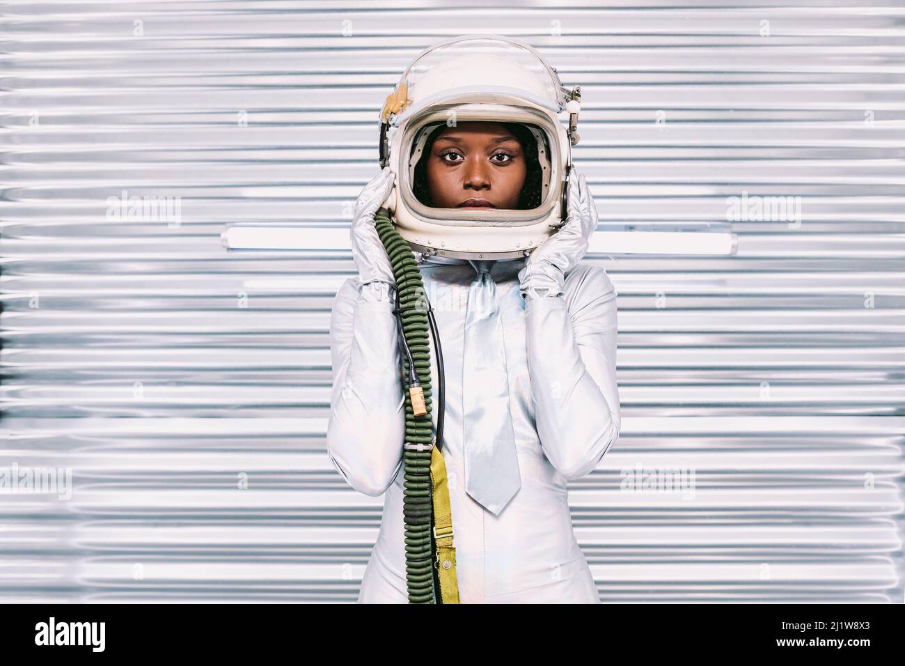 Ernste afroamerikanische Astronautin in weißem Raumanzügen mit Helm, der auf die Kamera schaut, während sie auf hellem Hintergrund im Raumschiff steht Stockfoto