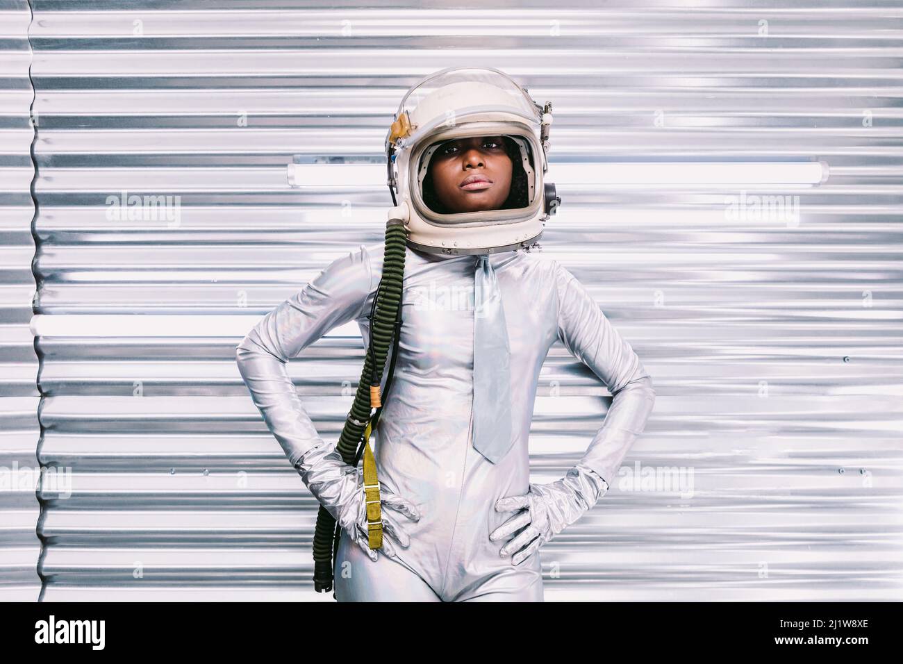 Ernste afroamerikanische Astronautin in weißem Raumanzügen mit Helm, der auf die Kamera schaut, während sie auf hellem Hintergrund im Raumschiff steht Stockfoto