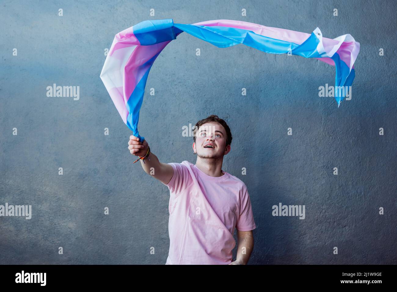 Anonymer Mann mit farbenfroher Transgender-Flagge mit Streifen, während er auf grauem Hintergrund in einem hellen Raum steht Stockfoto