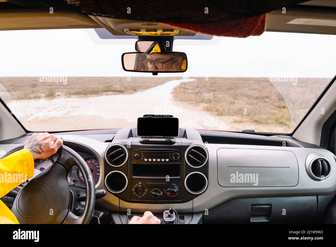 Crop anonymen männlichen Fahrer in Brillen spiegeln sich in den Spiegel, während der Fahrt modernen Automobil mit schwarzem Armaturenbrett auf der Straße auf dem Land Stockfoto
