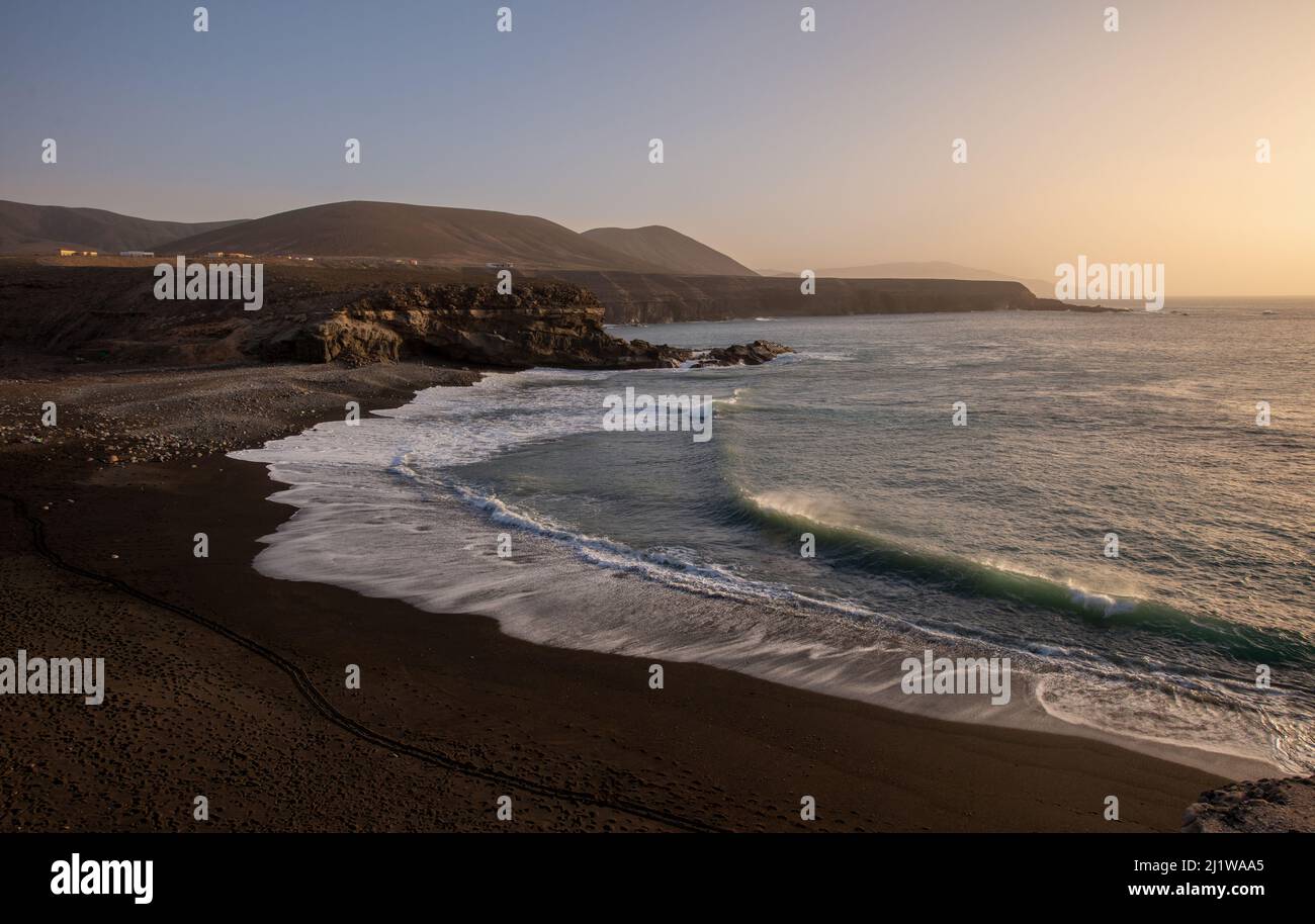 Malerische Meereslandschaft mit schäumenden Meereswellen, die den Sandstrand unter vulkanischen Formationen auf der Insel Fuerteventura waschen Stockfoto