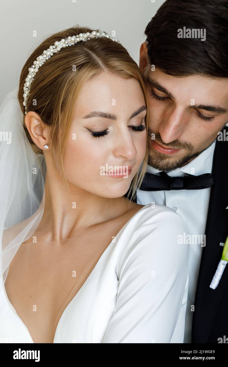 Ein stilvoller Bräutigam süß umarmt eine Braut in einem Brautkleid. Das Brautpaar umarmt sich im Zimmer und verbringt Zeit miteinander Stockfoto