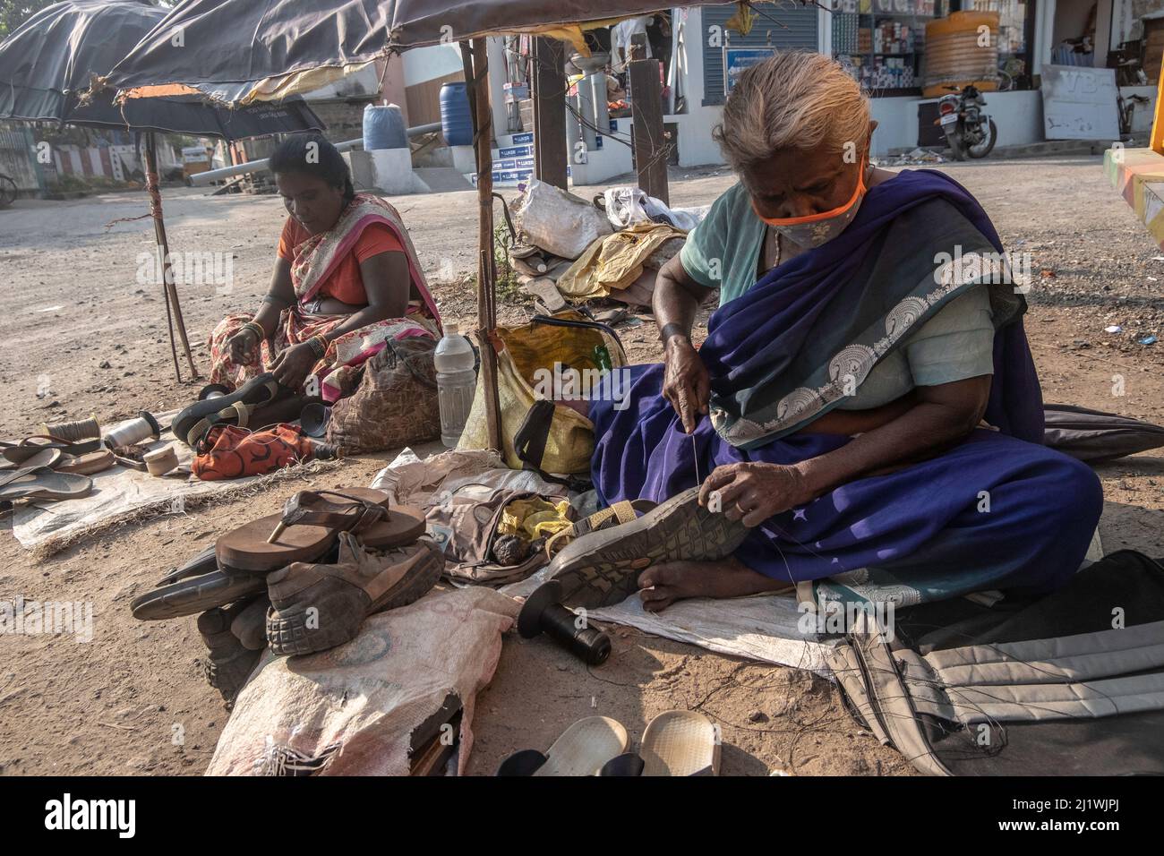 Schuhmacher repariert ein Paar Sandalen auf dem Marktplatz in Tiruvannamalai, Tamil Nadu, Indien Stockfoto