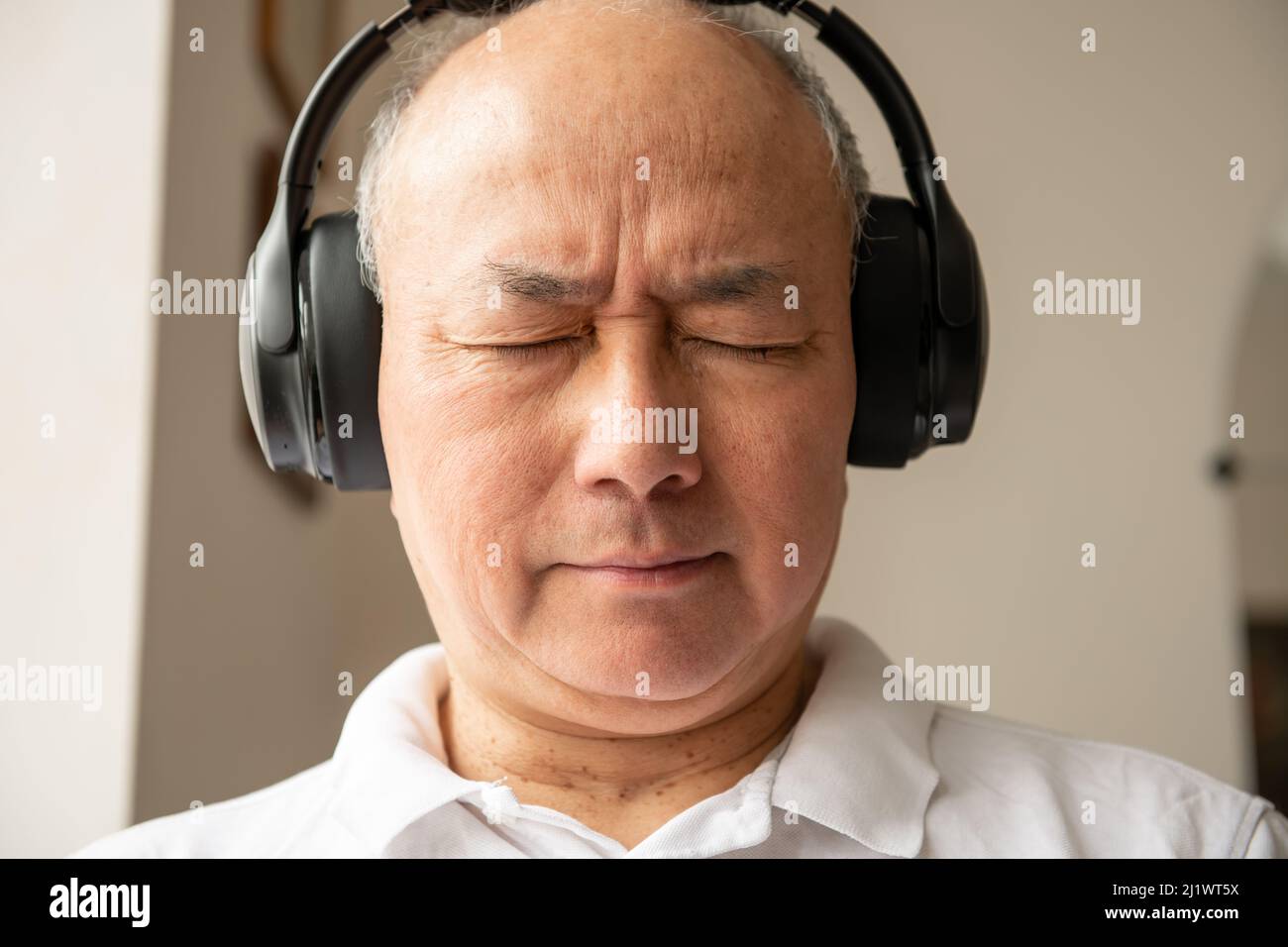 Ein gereifter Mann, der sich zu Hause entspannt und Musik mit einem Paar Kopfhörern hört. Stockfoto