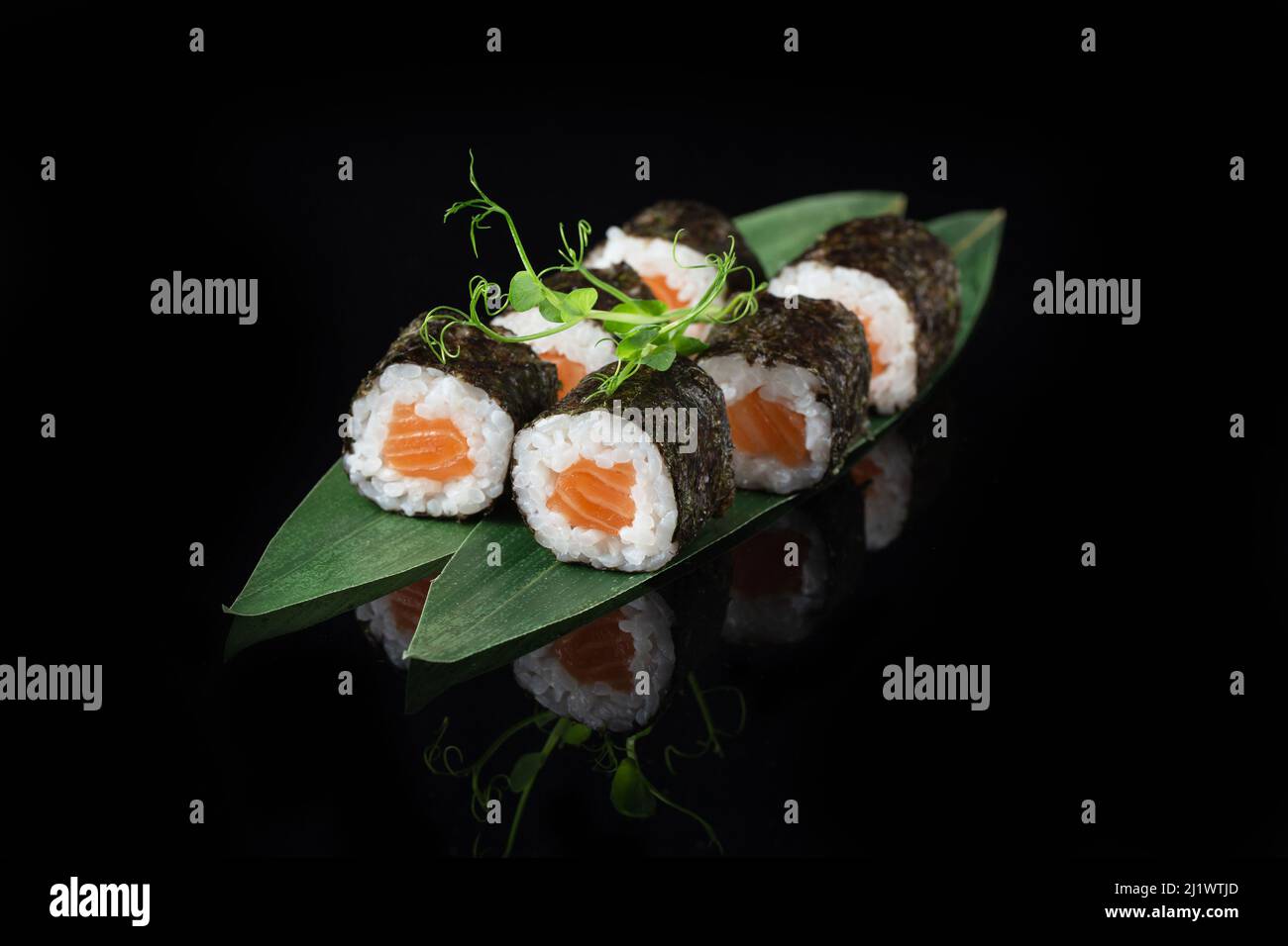 Traditionelle, köstliche, frische Sushi-Rolle auf schwarzem Hintergrund mit Spiegelung. Sushi-Rolle mit Reis, Nori, Frischkäse, Tobiko-Kaviar, Avocado. So Stockfoto