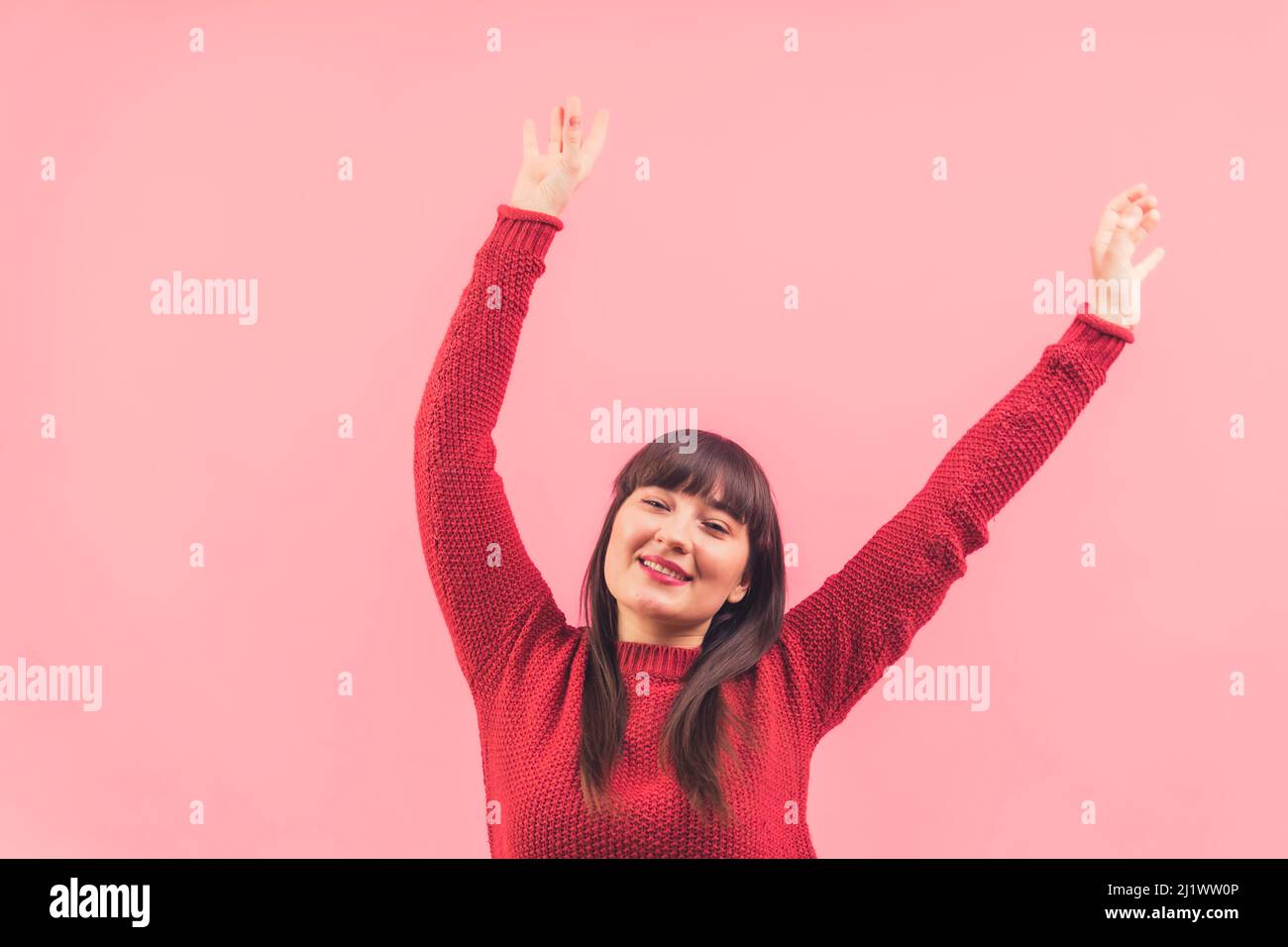 Voller Energie positive kaukasische Brünette wirft Hände in die Luft und lächelt über rosa Hintergrund. Studioaufnahme. Hochwertige Fotos Stockfoto