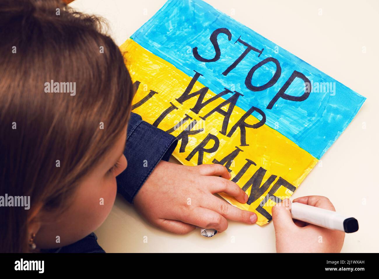 Das kleine ukrainische Mädchen zeichnet ein Bild mit der Flagge der Ukraine und dem Text STOP WAR IN DER UKRAINE. Russische Invasion der Ukraine. Stockfoto