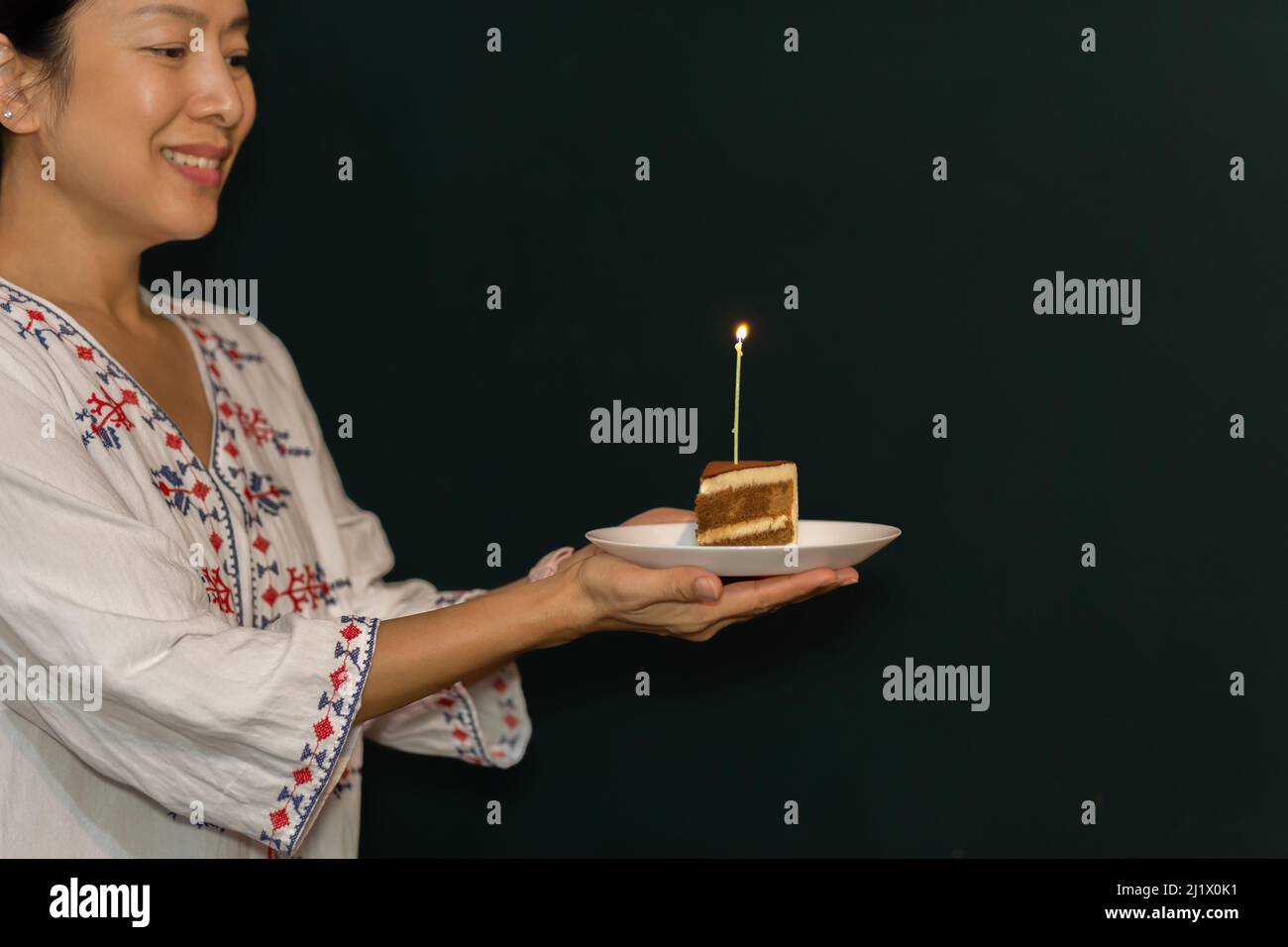 Frau Hand hält ein Stück Geburtstagskuchen auf dem Teller mit Kerze. Stockfoto