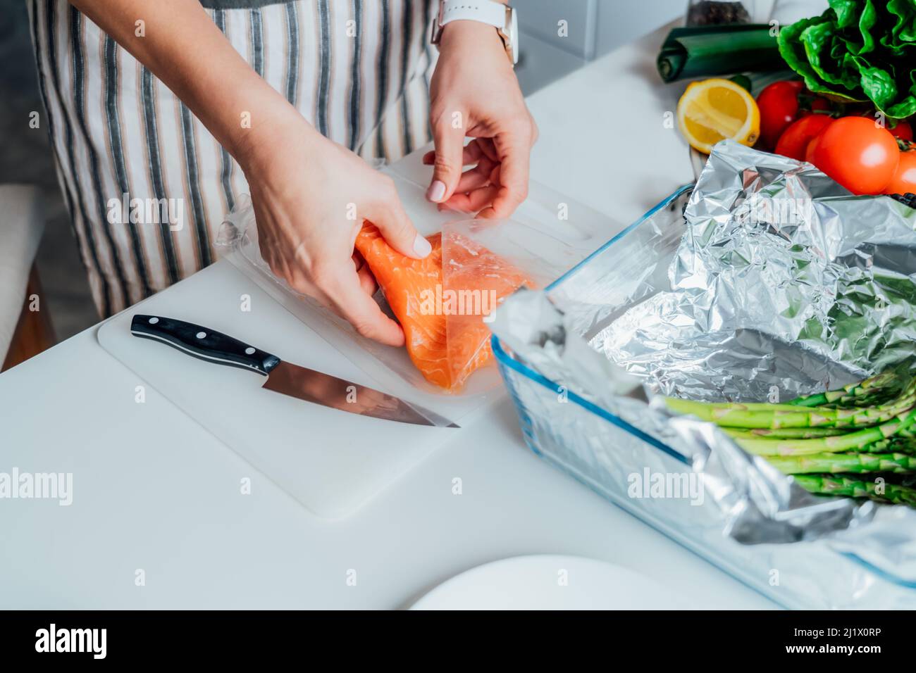 Gebackener Lachs mit grünem Spargel – Rezeptschritte. Schritt 1. Frau plant, frischen Lachs auf Schneidebrett zu schneiden. Schritt für Schritt Rezept. Gesundes Kochen Stockfoto