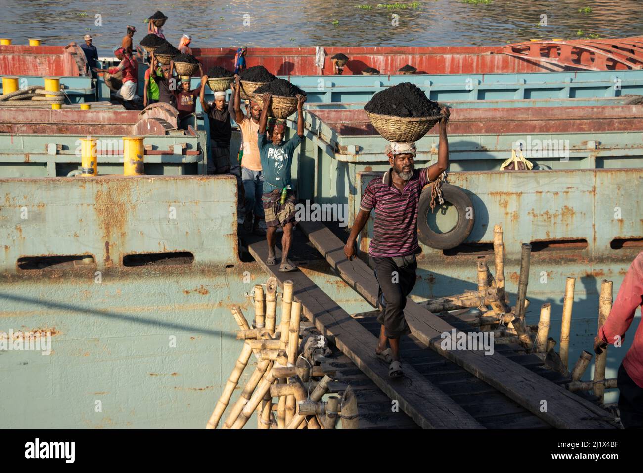 Dhaka, Dhaka, Bangladesch. 13. März 2022. Arbeiter transportieren Körbe voller Kohle auf ihren Köpfen, während sie Kohle von einem Frachtschiff in Dhaka entladen. Etwa 3,0 Prozent der Energie des Landes stammt derzeit aus Kohle. Am frühen Morgen beginnen die Arbeiter, Kohlen bis zum Sonnenuntergang zu entladen, sie verdienen $5 bis $7 Dollar pro Tag. Es gibt keine speziellen Schuhe an ihren Füßen und keine Handschuhe in ihren Händen, um Kohle von Frachtschiffen zu entladen. Außerdem stellen lange Arbeitszeiten unter der sengenden Sonne, massive Staubansammlungen und überhöhte Belastungen für die Arbeitnehmer ernste Gesundheitsrisiken dar. (Bild: © Stockfoto