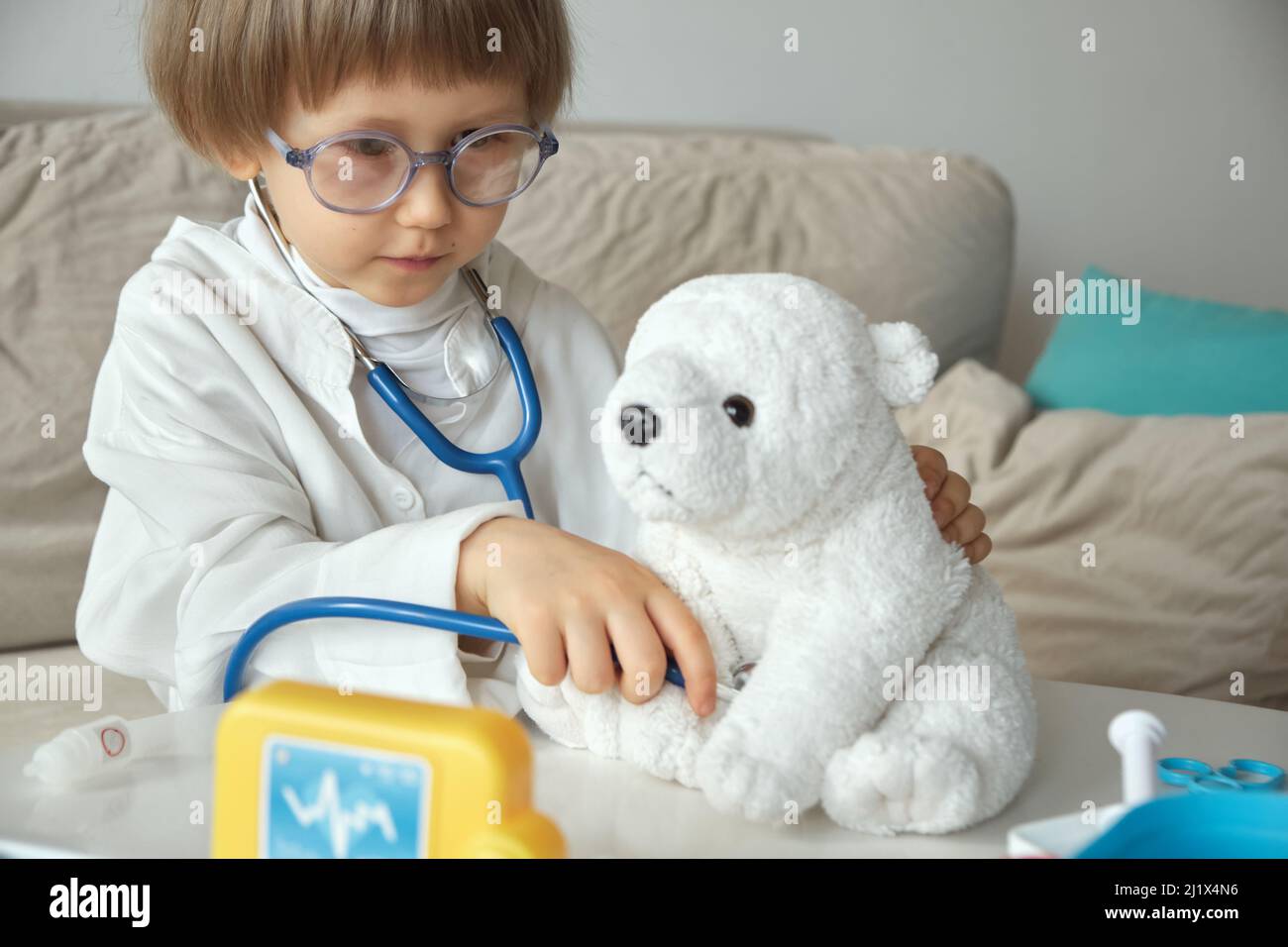 Kleiner Arzt im medizinischen Mantel mit Stethoskop spielen eine Untersuchung des Spielzeug-Teddybären Stockfoto