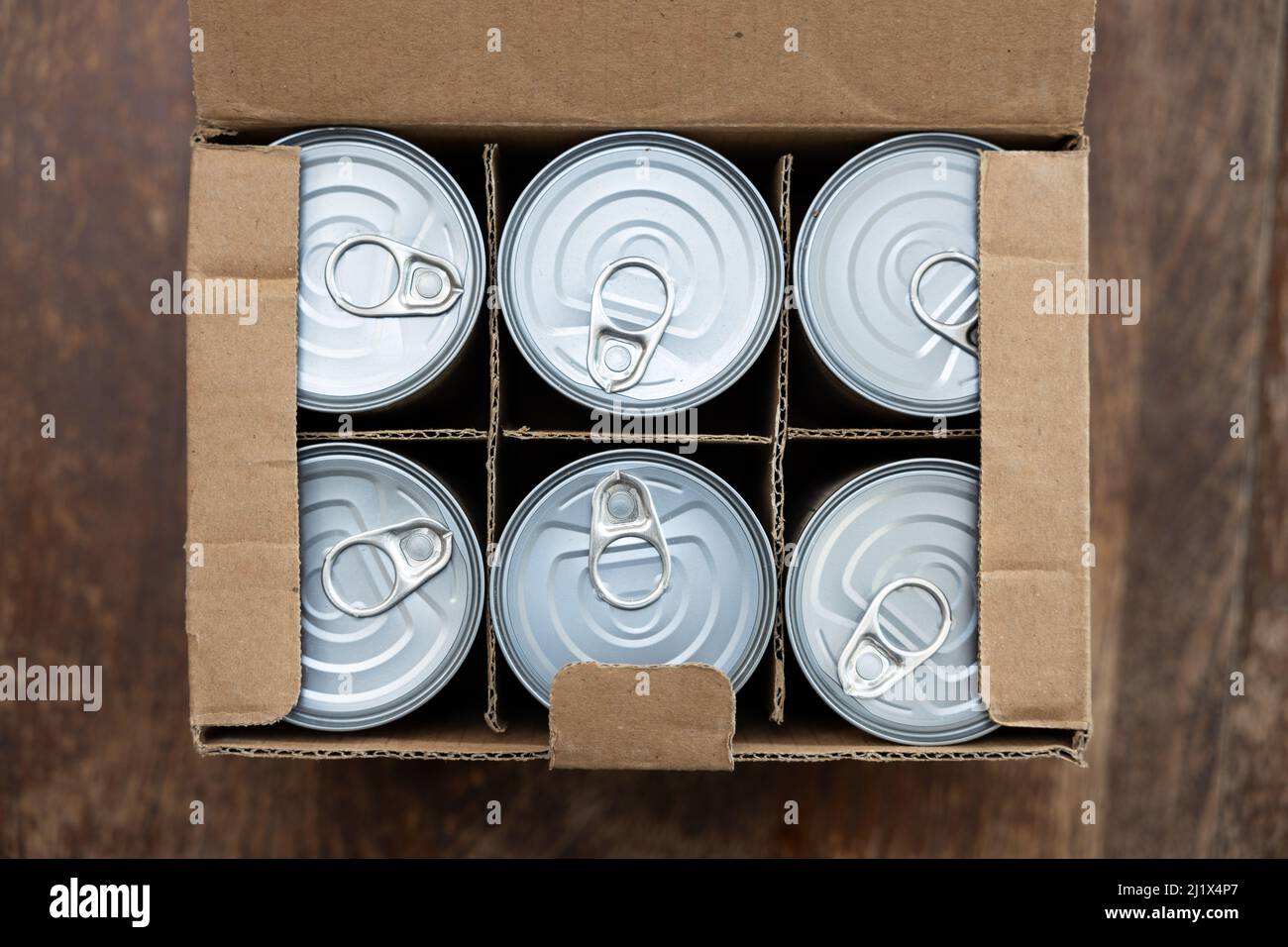 Lebensmitteldosen in einem offenen Karton auf einem Holztisch. Konzeptbild für Störungen der Lieferkette, Nahrungsmittelknappheit, Lagerbestände in Kriegszeiten. Stockfoto
