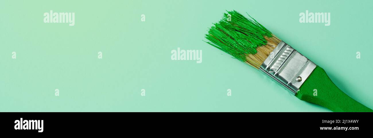 Ein grüner Pinsel mit etwas grüner Farbe, auf einem hellgrünen Hintergrund mit etwas Leerzeichen auf der linken Seite, in einem Panorama-Format als Webbanner oder zu verwenden Stockfoto