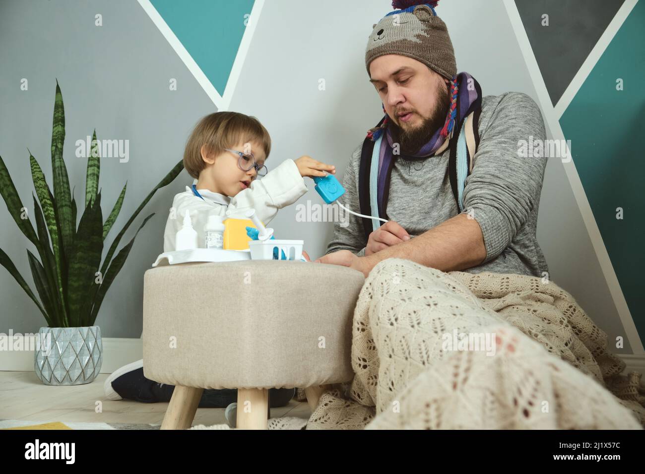 Vater und Kind spielen Klinik und Arzt, kleiner Junge in medizinischen Kleid mit Stethoskop behandelt Papa Stockfoto