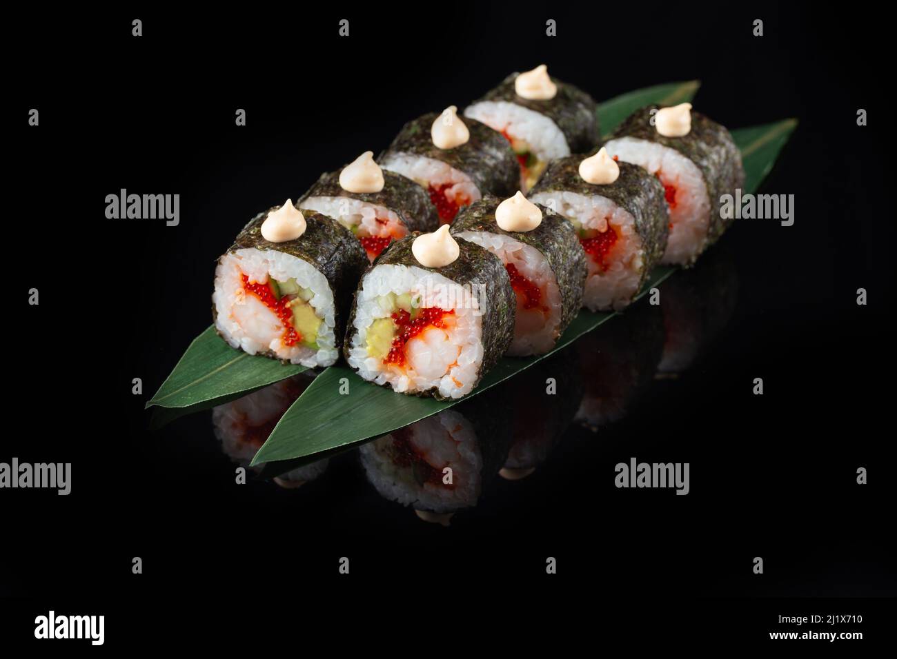Traditionelle, köstliche, frische Sushi-Rolle auf schwarzem Hintergrund mit Spiegelung. Sushi-Rolle mit Reis, Nori, Frischkäse, Tobiko-Kaviar, Avocado. So Stockfoto
