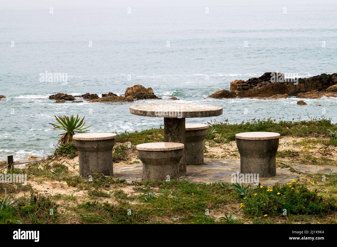 Steintisch und Bänke mit Meerblick, romantische Szenen am Meer. Blick auf die Sandklippen am Strand auf das Meer. Essen mit Meerblick. Steintisch. Stockfoto