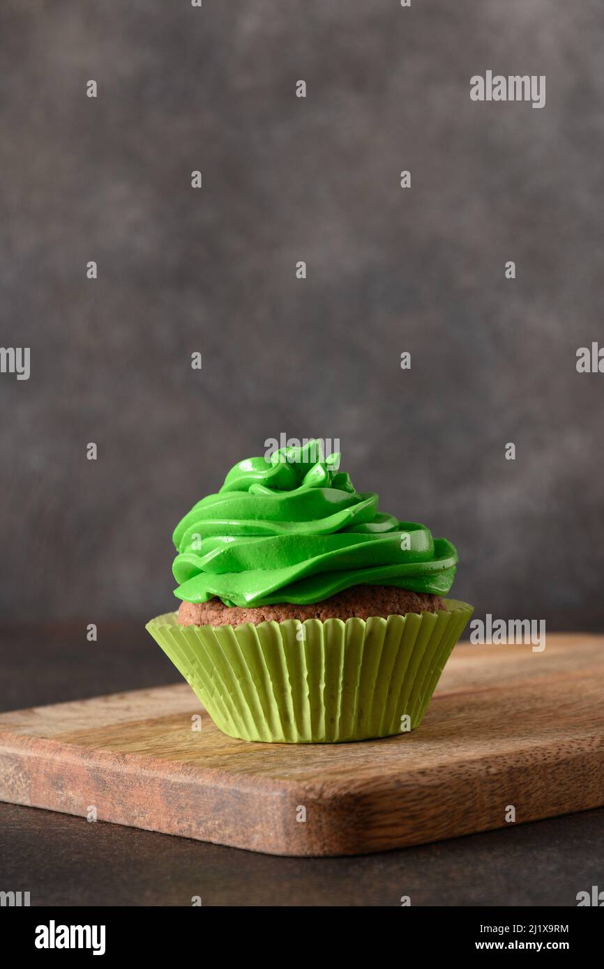 Leckerer hausgemachter Cupcake aus Schokolade mit grüner Schlagsahne auf braunem Hintergrund. Vertikales Format. Nahaufnahme. Stockfoto
