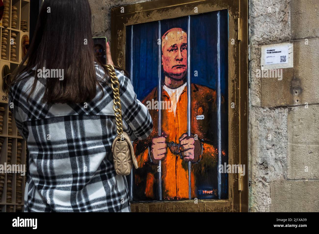 Barcelona, Spanien. 28. März 2022. Ein Pendler fotografiert ein Graffiti des italienischen Stadtkünstlers „TVBoy“, Salvatore Benintende, mit dem Titel „der Traum“, auf dem der russische Präsident Wladimir Putin aus Protest gegen die anhaltenden russischen Angriffe im Gefängnis und hinter Gittern abgebildet ist.Quelle: Matthias Oesterle/Alamy Live News Stockfoto