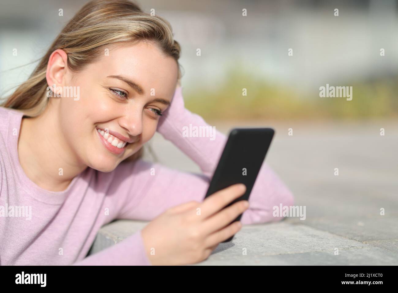 Fröhlicher Teenager, der auf der Straße mit einem Smartphone lächelt Stockfoto