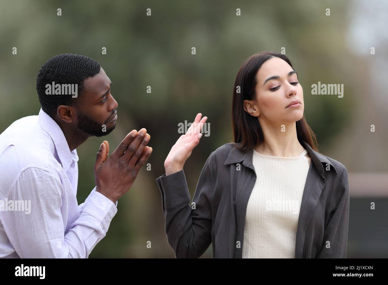 Mann mit schwarzer Haut bettelt verzeihen und kaukasische Frau lehnt ihn in einem Park Stockfoto