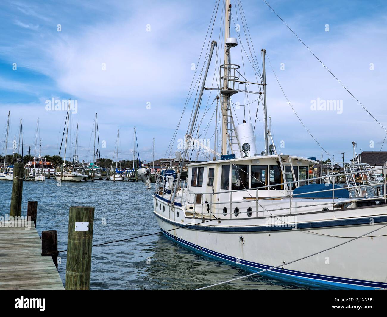 Weißes kommerzielles Garnelenfischboot mit Mast und Takelage ist mit Seilen am Dock in einer Marina befestigt. Stockfoto