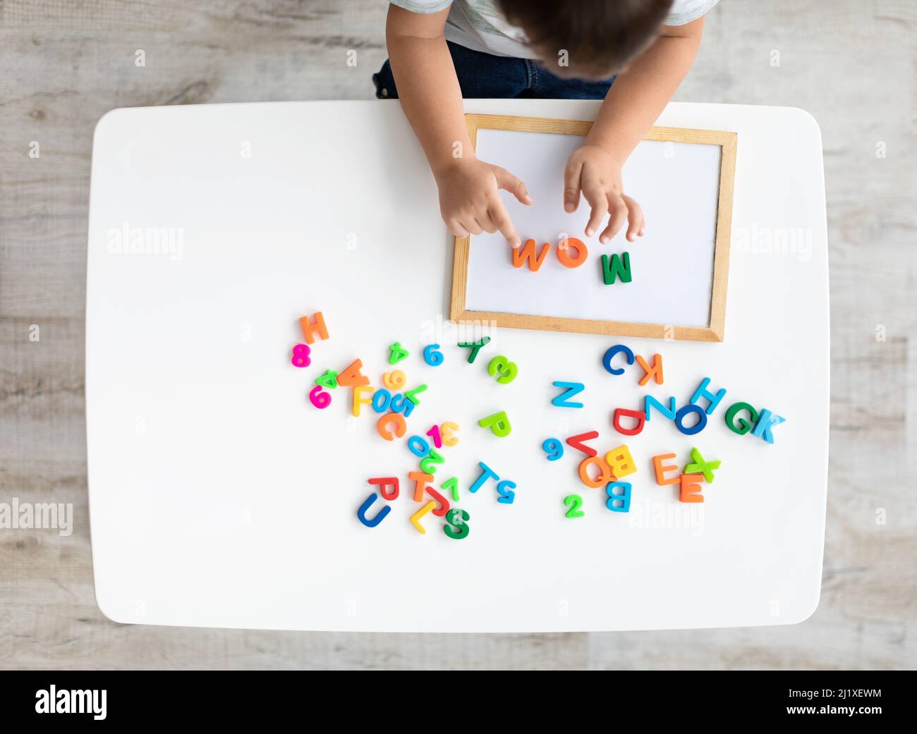 Frühe Entwicklung und Vorbereitung auf die Schule. Draufsicht des kleinen Kindes, das Wort MUTTER mit bunten Buchstaben macht, leerer Raum Stockfoto