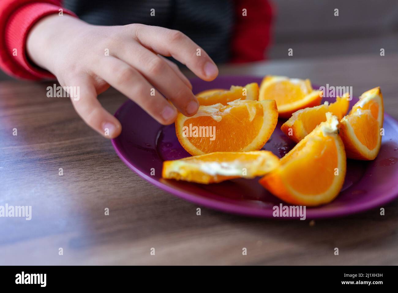 Der Junge hält eine Scheibe Orange in der Hand. Eine Platte aus geschnittenem Orange. Stockfoto