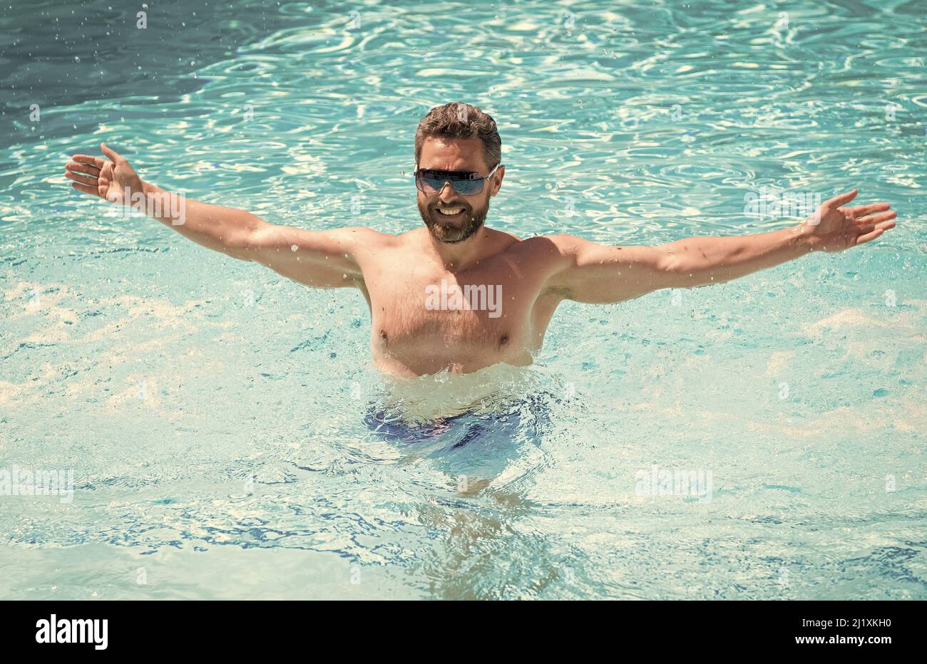 Glücklicher, gutaussehender Mann in einer Brille, der im Sommer, im Urlaub im Pool schwimmte Stockfoto