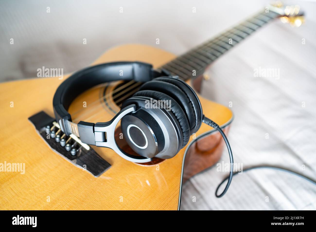 Akustische Gitarre und Ohrhörer auf dem Bett Stockfoto