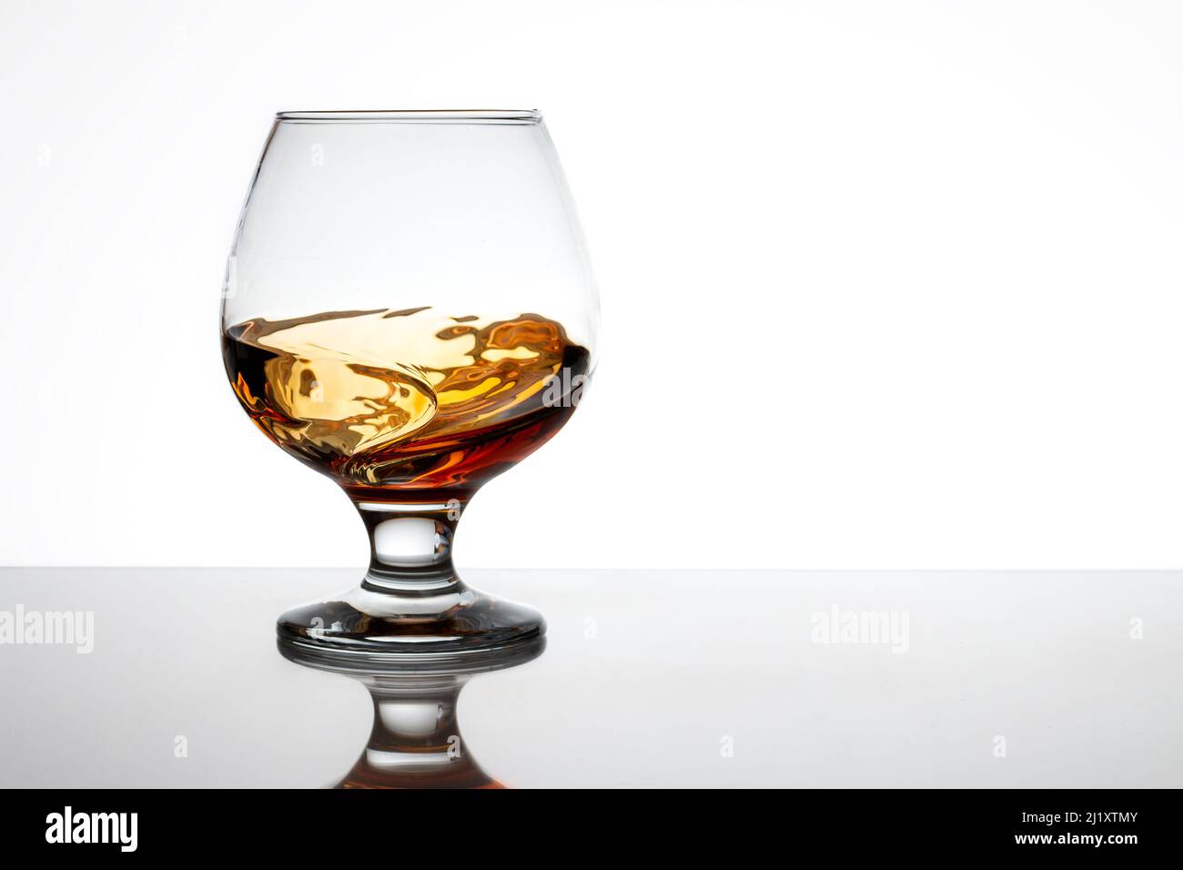 Ein Glas Brandy in Bewegung, das sehr attraktive Wellen bildet. Der Hintergrund ist weiß und der Glasboden wird auf der Oberfläche reflektiert. Stockfoto