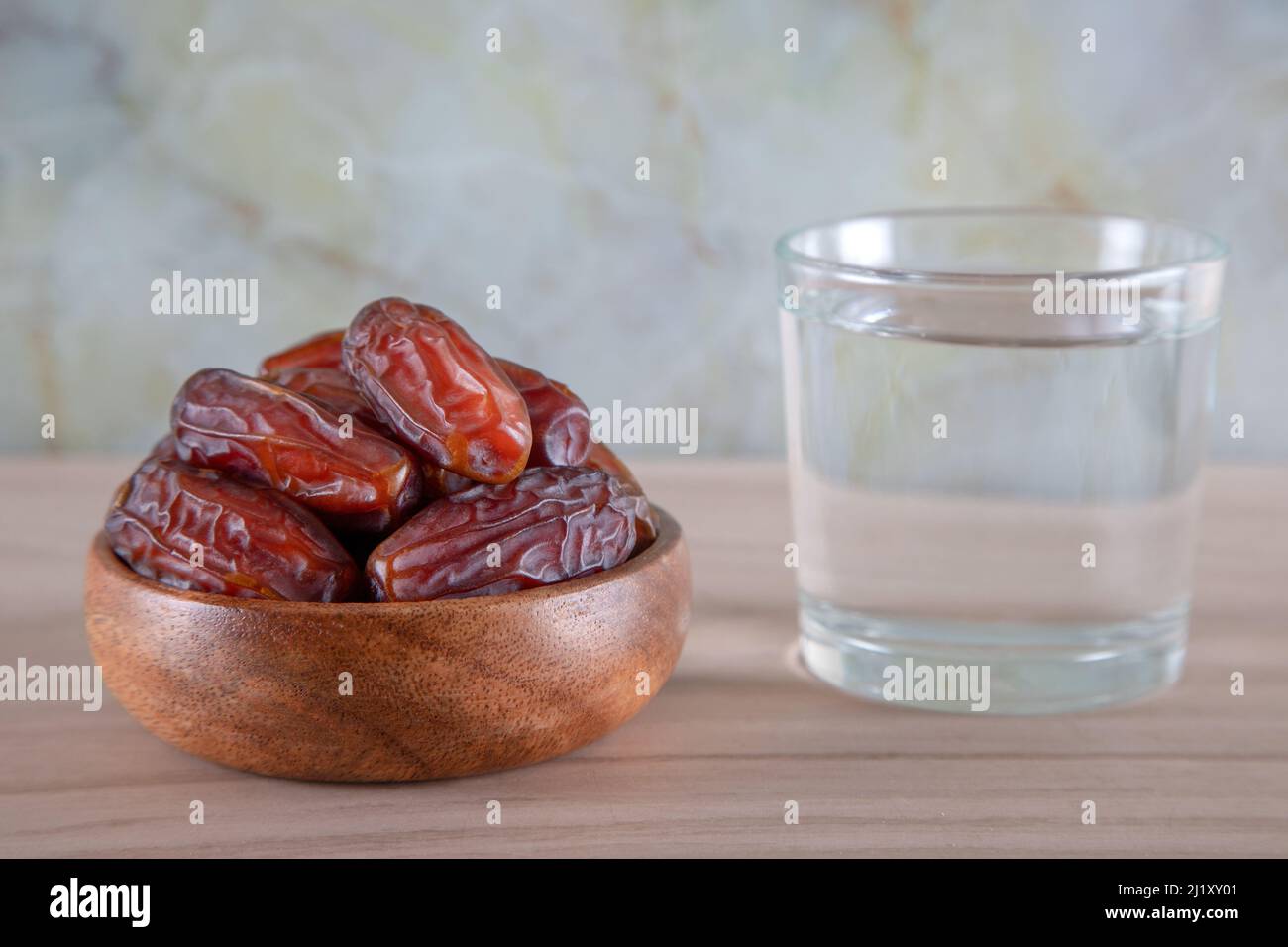 Glas Wasser mit einer Schale Datteln Obst auf einem hölzernen Hintergrund.Muslime brechen das Fasten mit Wasser und Datteln Stockfoto