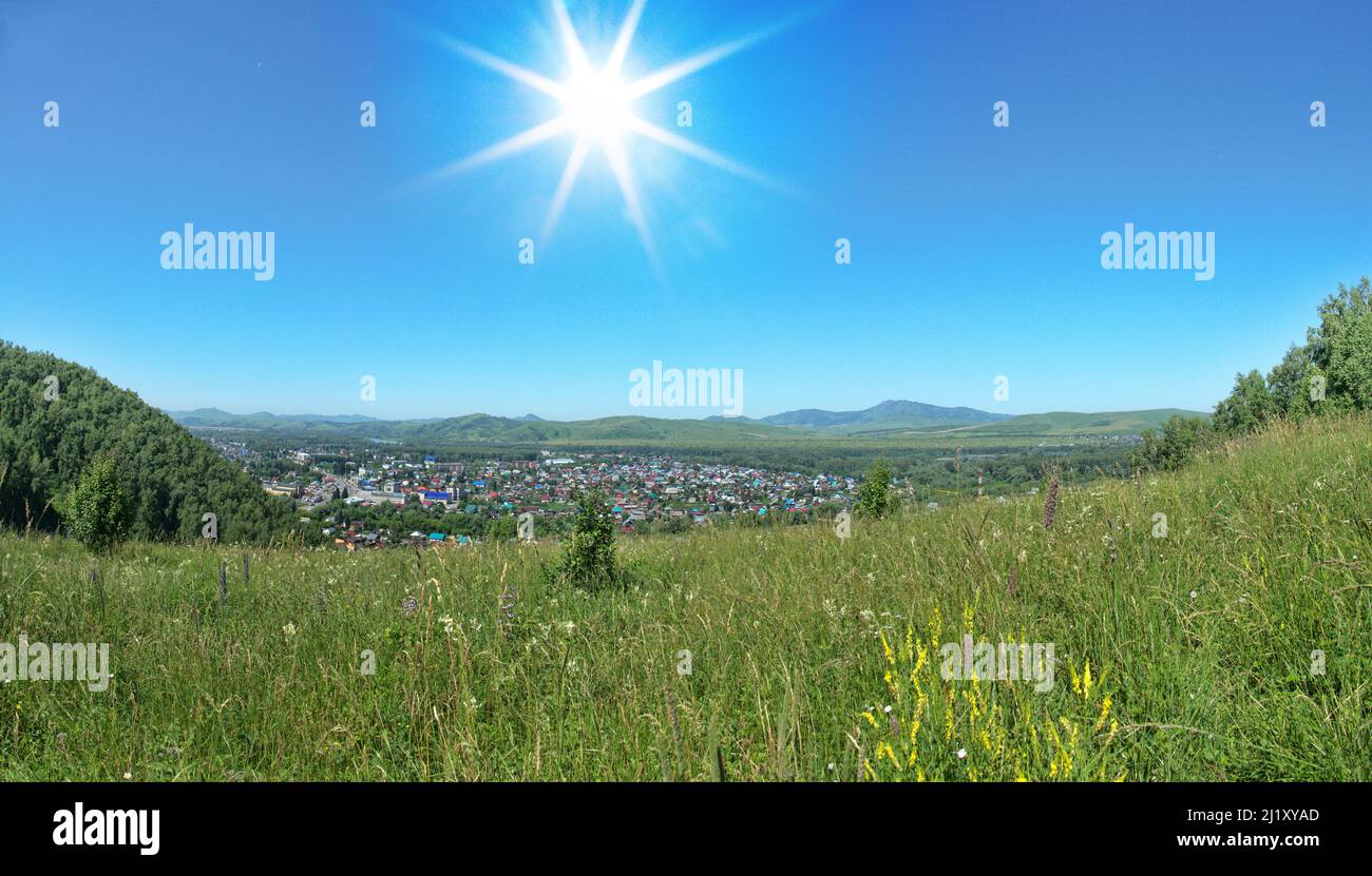 Runde Stadt im Tal ist erfolgreich in Bergsattel platziert. Bergsteppe im Vordergrund. Altai. Die anthropogenen Auswirkungen kleiner Städte sind minimal. Stockfoto