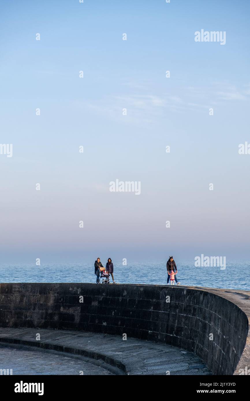 Menschen, die entlang der Hafenmauer bei Lyme Regis, Großbritannien (Mar22) Stockfoto