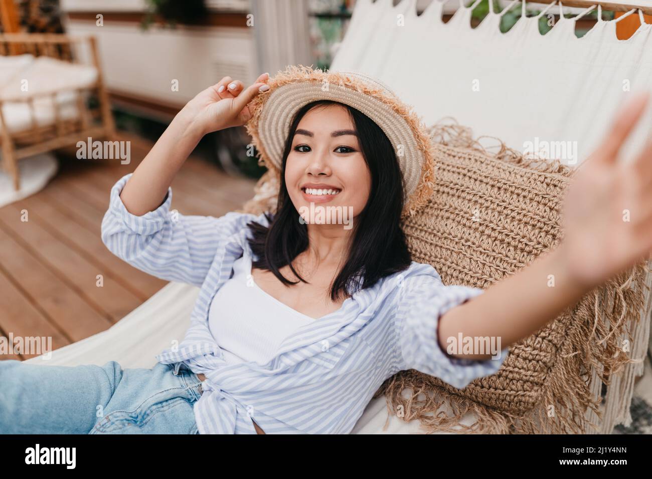 Lächelnde junge asiatische Frau, die in der Hängematte in der Nähe des Wohnwagens liegt und Selfie auf dem Campingausflug auf dem Land macht Stockfoto