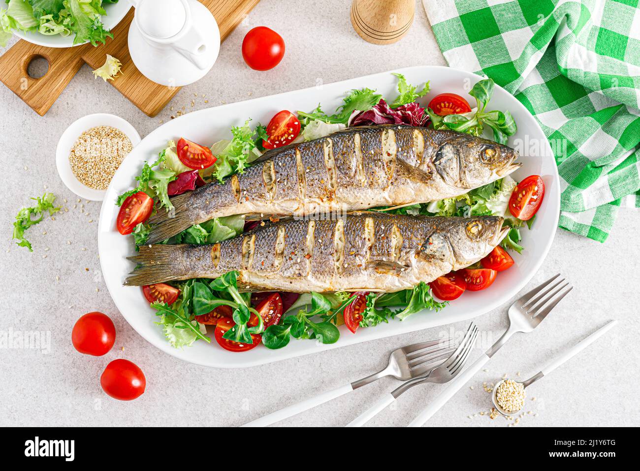 Seebarsch oder Seebarsch Fisch geröstet und frisches Gemüse Salat aus Tomaten und Salat, gesunde Ernährung zum Mittagessen, Draufsicht Stockfoto