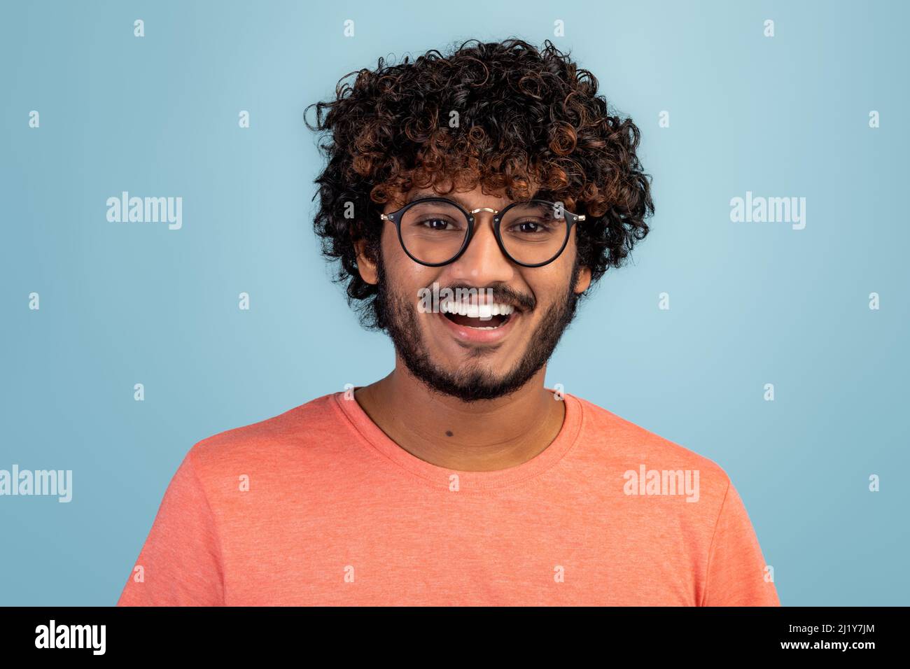 Glücklicher hindu-Kerl in Brillen, der auf Blau posiert Stockfoto