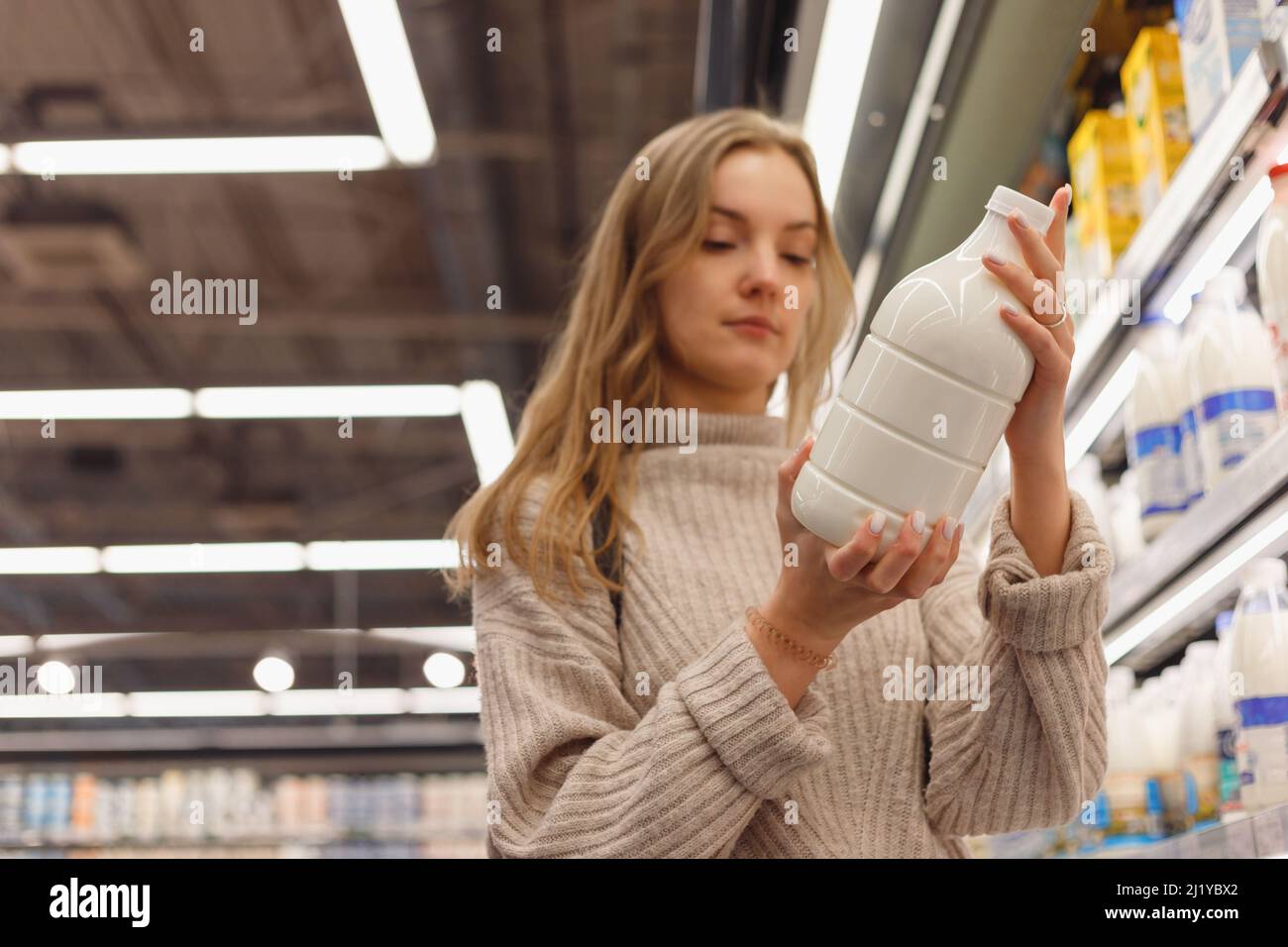 Lebensmittelgeschäfte. Frau lesen Milchflasche im Laden, der in der Nähe des Regals mit Milchprodukten im Supermarkt steht. Lady Buyer Kaufbedarf Stockfoto