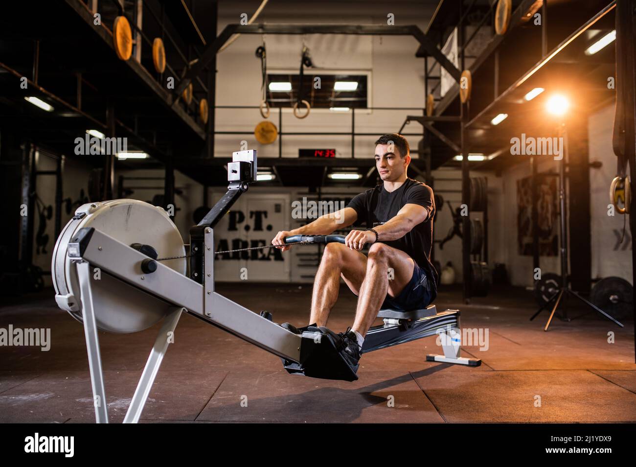Ein attraktiver muskulöser junger Mann in einem voll ausgestatteten Fitnessstudio trainiert den ganzen Körper individuell auf dem Indoor-Rudergerät Stockfoto