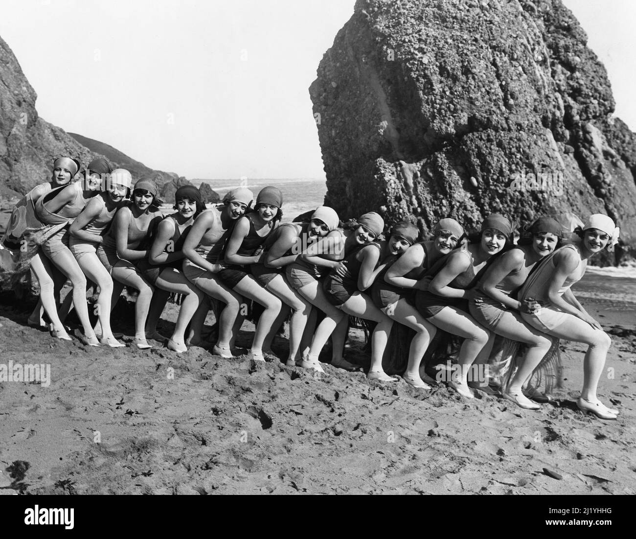 Eine Gruppe junger Frauen in Badeanzügen und Kopfhüllen hockt in einer engen Schlange am Strand für ein Porträt. Stockfoto
