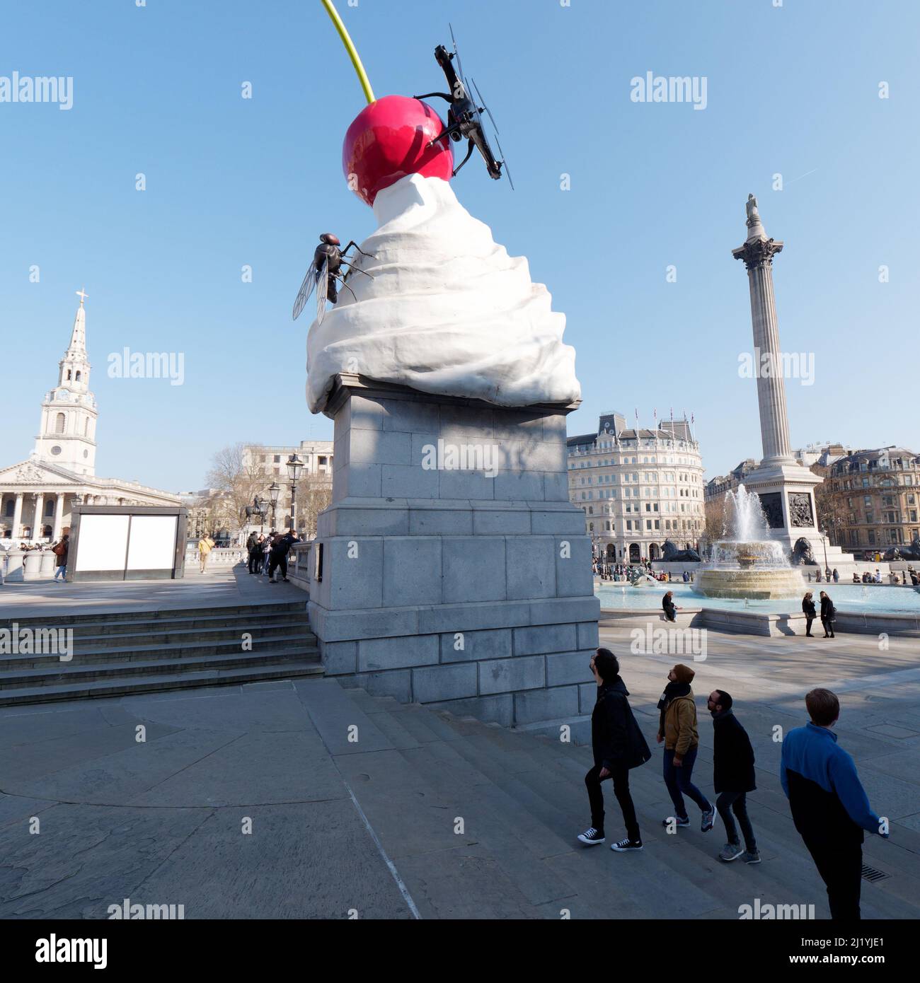London, Greater London, England, März 08 2022: Touristen blicken auf die Trafalgar Squares Vierter Sockel einer Schlagsahne, Kirsche und Fliegenskulptur. Stockfoto
