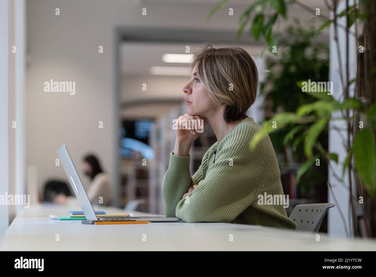 Reife Studentin, die in der Universitätsbibliothek sitzt, Pause vom Online-Lernen nimmt Stockfoto